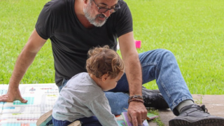Niño pequeño leyendo un libro con un adulto, representando la alfabetización temprana en el hogar.